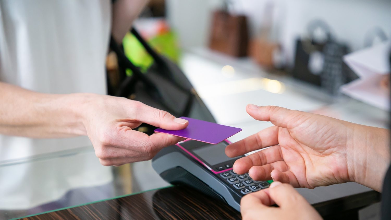 Customer giving credit card to cashier over desk with pos terminal for payment. Cropped shot, closeup of hands. Shopping concept
